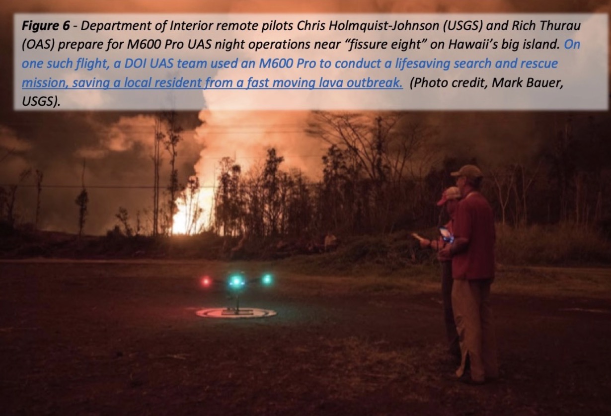 Two peole looking at. drone while. fire rages off in the distance. 