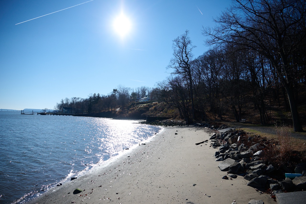 A beach with calm blue waters and a bright sun in a bloe skey. 