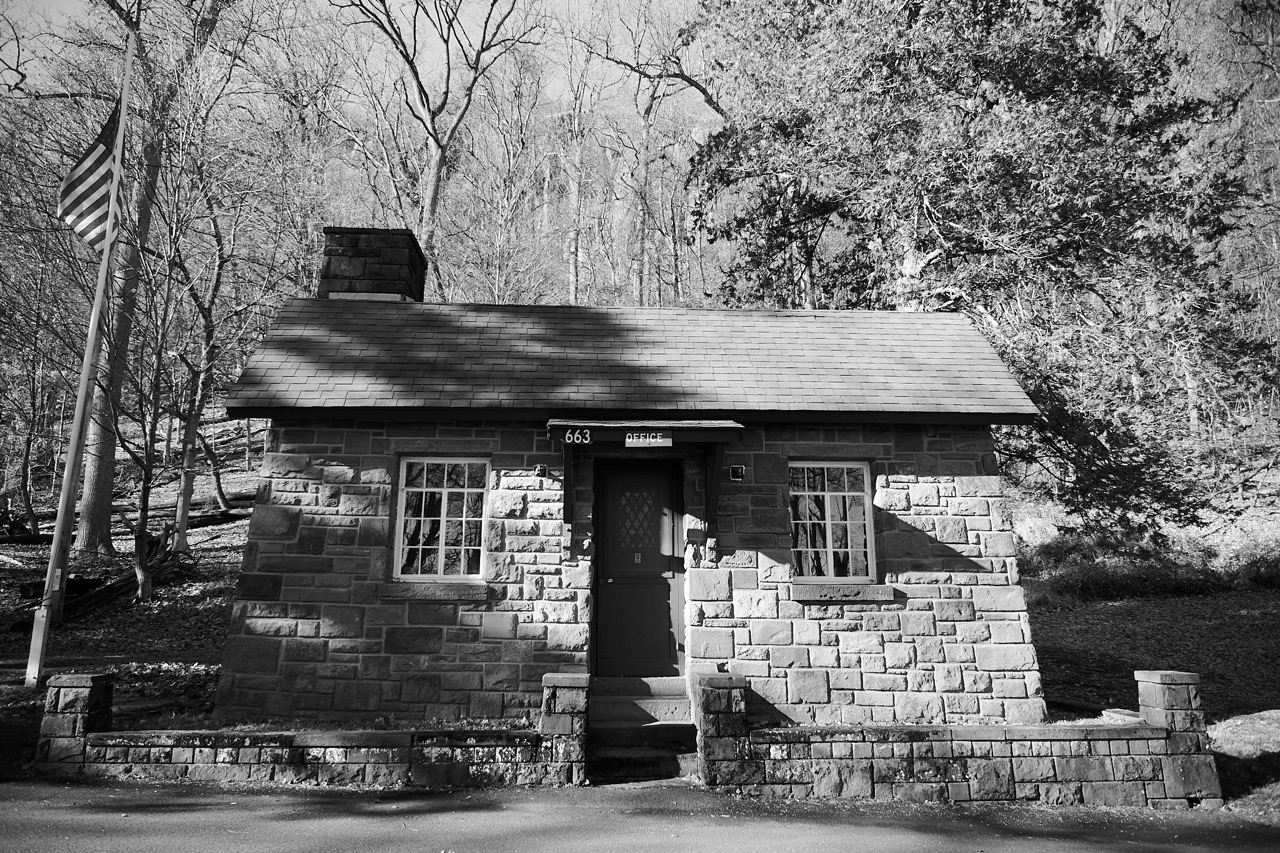 A stone buliding set against the woods, in black and white. 