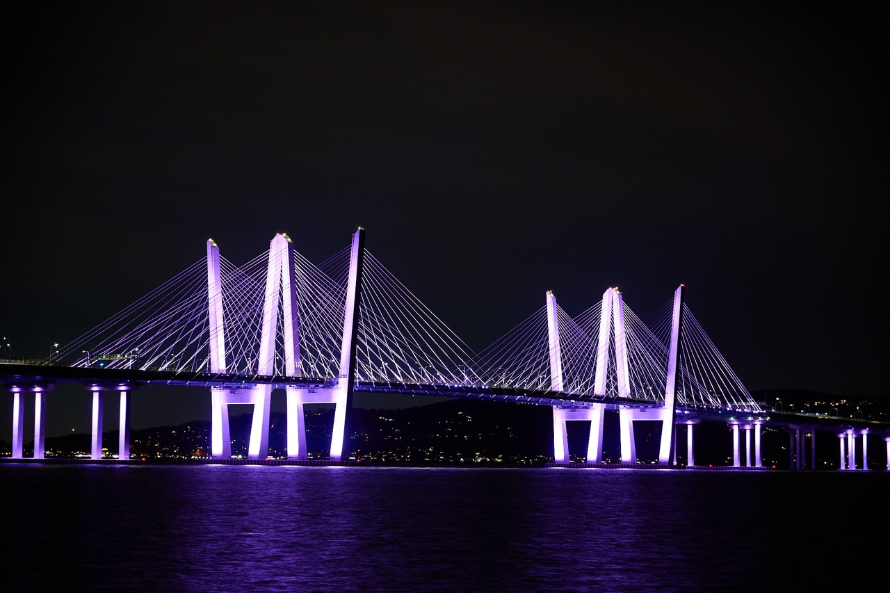 The Mario Cuomo Bridge at night with the sttucture lit in purple light, againast a black sky.