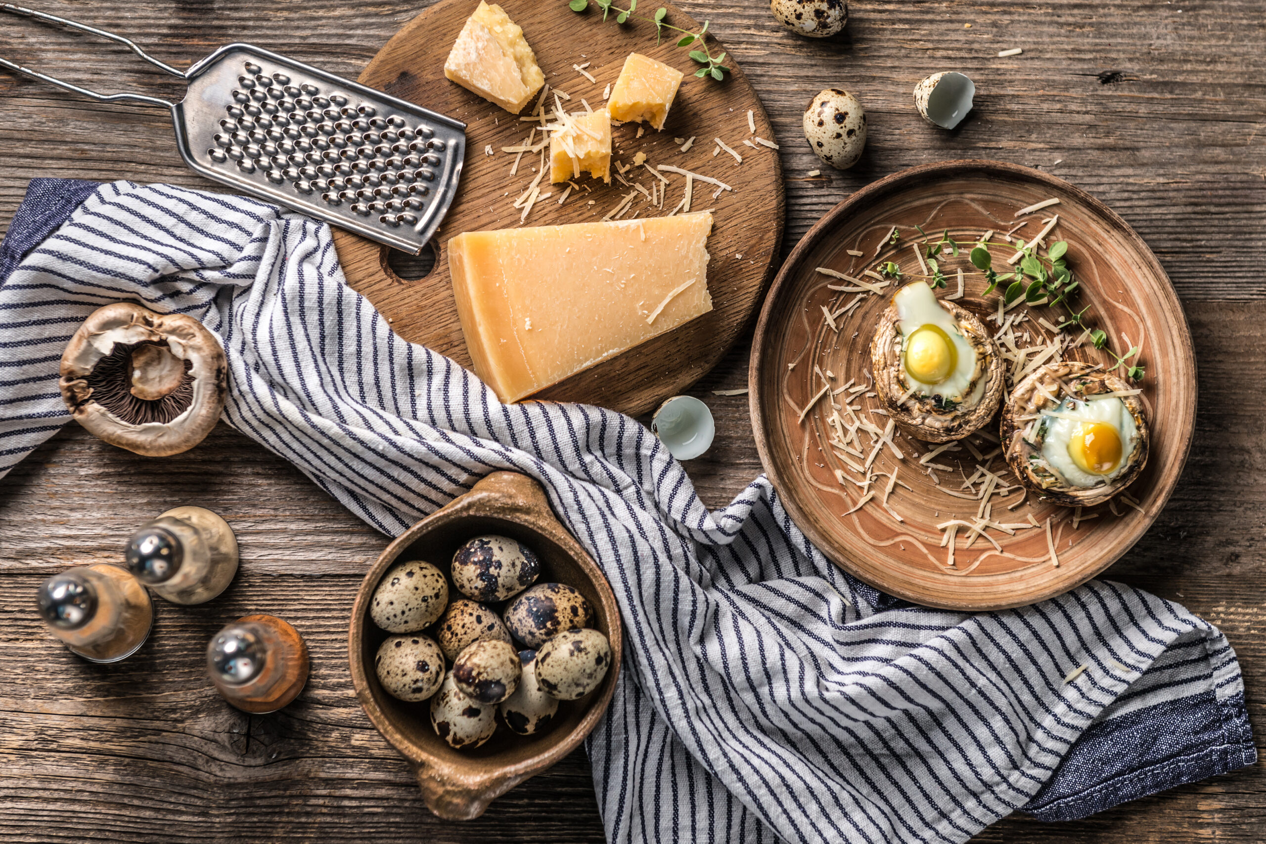 Stuffed mushrooms with quail eggs and parmesan cheese with food ingredients on aged wooden background, top view.